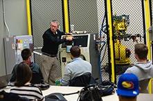 Students in a class observing a professor teach about mechanical equipment.