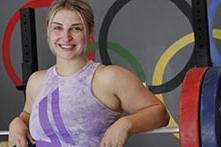 image of Kate Nye standing in a weight room with the Olympics symbol behind her