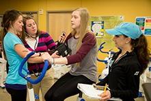 A young woman on a fitness bike with three women performing fitness evaluations on her.